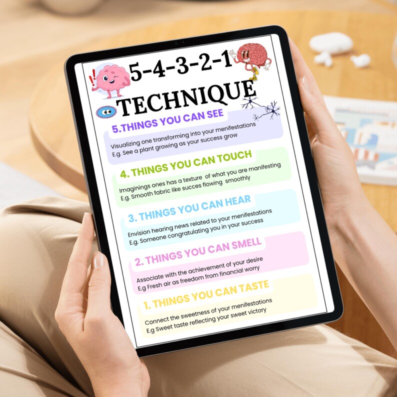 May include: A tablet displays a colorful infographic titled "5-4-3-2-1 TECHNIQUE." The graphic lists five sensory-based steps for manifestation, including things to see, touch, hear, smell, and taste. The tablet is held by a person.