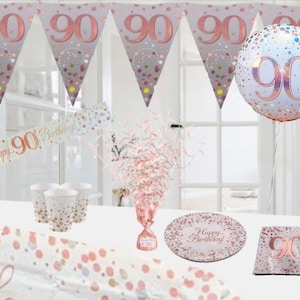 May include: Rose gold 90th birthday party decorations. The set includes a banner, a balloon, plates, cups, napkins, and confetti. The banner says "Happy 90th Birthday".