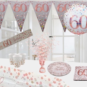 May include: Rose gold 60th birthday party decorations. The set includes a banner, a balloon, a table runner, plates, napkins, cups, and a centrepiece. The decorations feature a rose gold and white confetti pattern with the number 60.