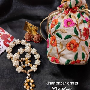 May include: A collection of handcrafted jewellery and accessories. Features a white beaded necklace with a gold pendant, gold and red earrings, and a floral embroidered pouch. The image also displays the text "kinaribazar crafts" and a WhatsApp number.
