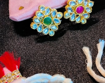 May include: Two gold-tone rings with a floral design. One ring has a green gemstone in the center, and the other has a pink gemstone in the center.
