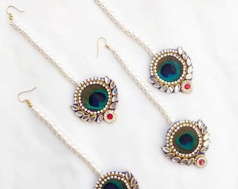 May include: Three sets of peacock feather earrings with pearl chains. Each earring features a round blue and green peacock feather design with gold accents and clear rhinestones. The earrings are attached to a white pearl chain.
