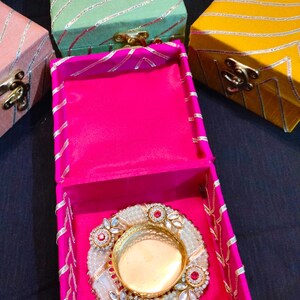 Könnte beinhalten: Ein dekoratives Box-Set in Pink, Grün und Gelb mit einem goldenen und weißen, mit Schmuck besetzten Kerzenhalter im Inneren. Die Boxen sind aus Stoff mit einem gestreiften Muster.