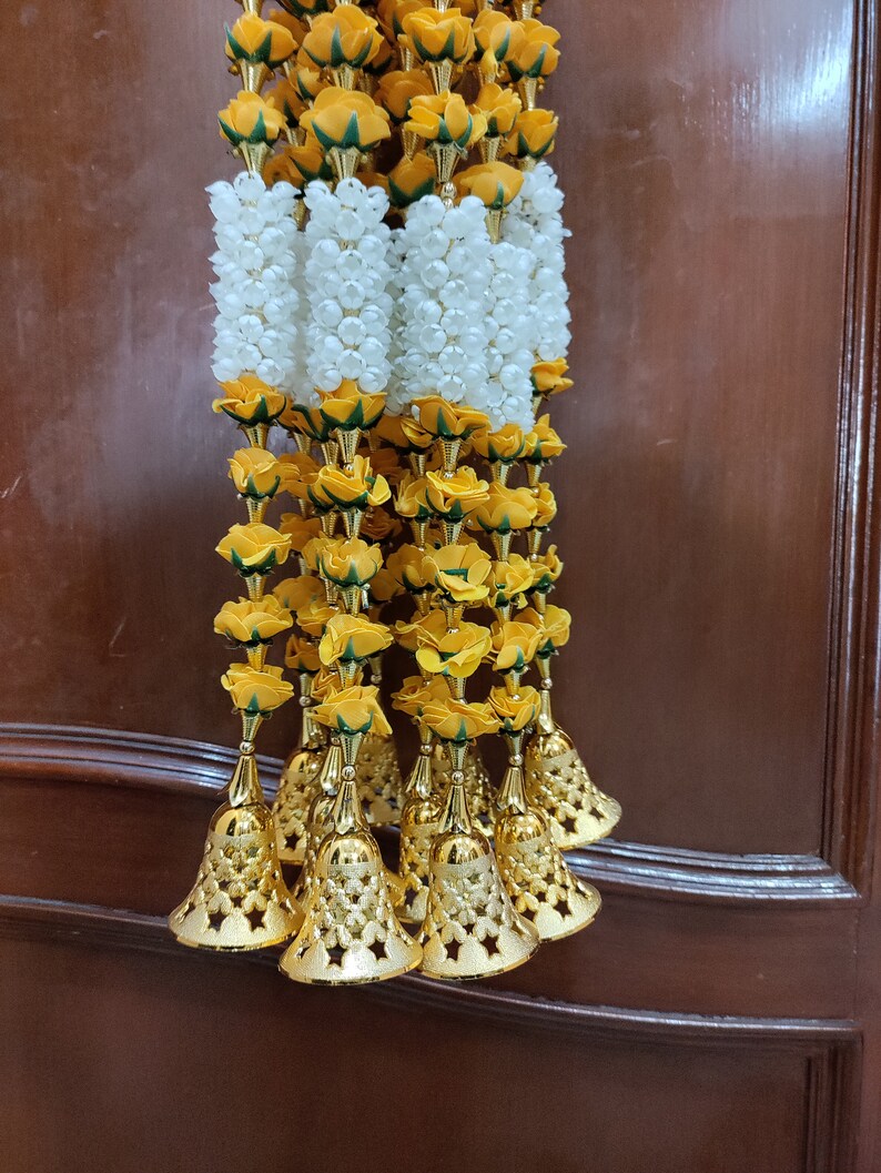 May include: A garland of yellow and white artificial flowers with gold bells hanging from the bottom.