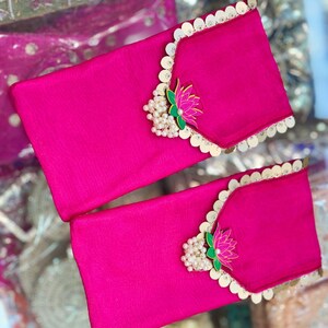 May include: Two pink fabric envelopes with gold and pearl embellishments. Each envelope has a decorative lotus flower design with green leaves.