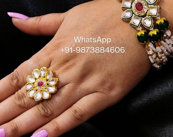 May include: A gold ring with a white and red flower design. The ring is on a person's finger. The person is also wearing a gold bracelet with a white and green flower design. The bracelet has white beads and green stones. The text "WhatsApp +91-9873884606" is visible in the image.
