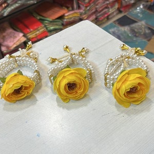 May include: Three white pearl bracelets with yellow flower accents. The bracelets are made of white pearls and have a gold clasp. Each bracelet has a yellow flower attached to the center.
