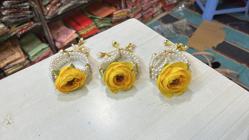 May include: Three white pearl bracelets with yellow flower accents. The bracelets are made of white pearls and have a gold clasp. Each bracelet has a yellow flower attached to the center.