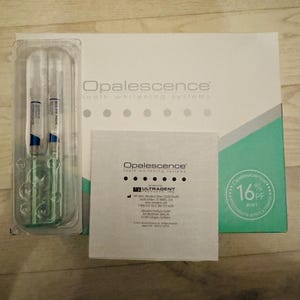 Peut inclure: Une boîte blanche et sarcelle de systèmes de blanchiment des dents Opalescence avec un emballage blister en plastique transparent contenant deux seringues. Une carte d'instructions carrée blanche avec du texte noir est placée devant la boîte.