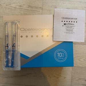 Peut inclure: Un kit de blanchiment dentaire Opalescence comprenant une boîte blanche et bleue, deux seringues bleues dans un emballage plastique transparent et une notice blanche. La boîte porte le texte Opalescence tooth whitening system et 10% PF.