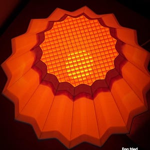 May include: An orange sunset lamp with a grid-like centre and a scalloped edge. The lamp is lit, emitting a warm glow. The text "Egg fried sunset lamp" is visible in the lower right corner.