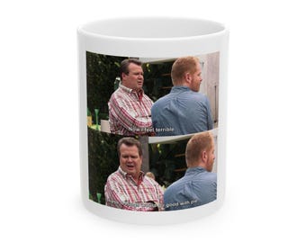 May include: White ceramic mug featuring a scene from the TV show Modern Family. The mug displays two panels with the characters Mitchell and Cameron, with the text "Now I feel terrible" and "These feelings would go good with pie."