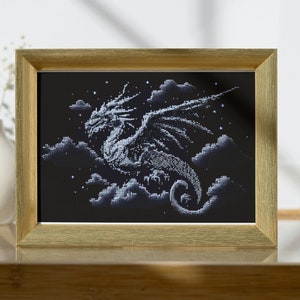 Könnte beinhalten: Gerahmtes Kunstwerk mit einem detaillierten, pixeligen Drachen im Flug vor einem sternenklaren Nachthimmel. Der Drache ist in Weiß- und Grautönen gehalten, mit Wolken, die Tiefe verleihen. Der Rahmen ist goldfarben.