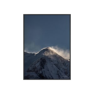 May include: A snowy mountain peak with a wispy cloud of snow blowing off the top, against a blue sky.