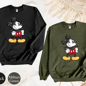 May include: Black and military green sweatshirts with a cartoon drawing of Mickey Mouse on the front.