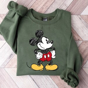 May include: A green sweatshirt with a black and white sketch of Mickey Mouse wearing red shorts and yellow shoes.