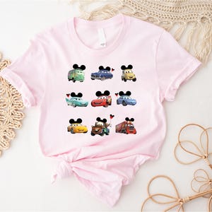 Puede incluir: Camiseta rosa con un gr&aacute;fico de nueve personajes de Cars, incluyendo Rayo McQueen, Mate y la gr&uacute;a. Cada personaje tiene orejas de Mickey Mouse.