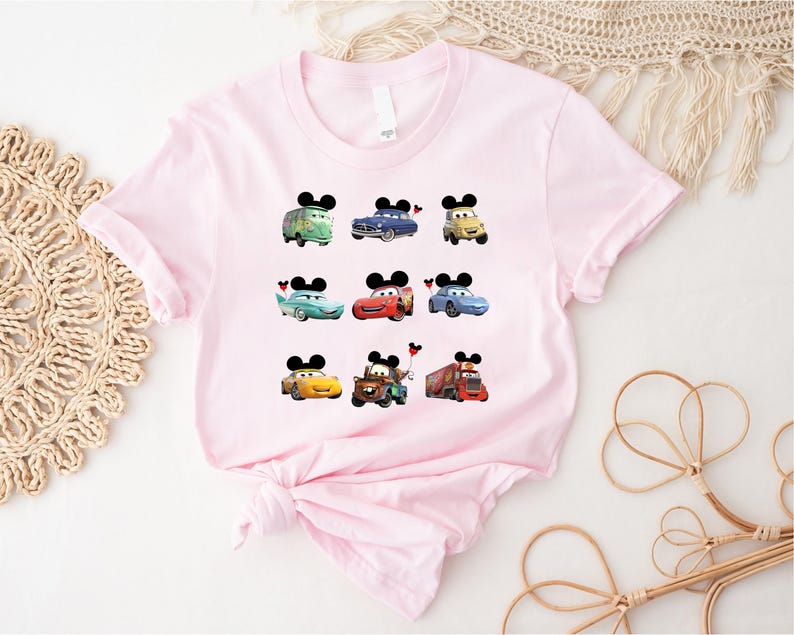 Puede incluir: Camiseta rosa con un gr&aacute;fico de nueve personajes de Cars, incluyendo Rayo McQueen, Mate y la gr&uacute;a. Cada personaje tiene orejas de Mickey Mouse.