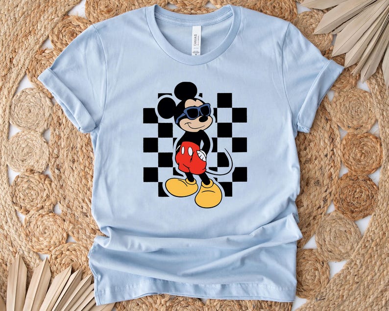 May include: Light blue t-shirt with a black and white checkered pattern and a cartoon image of Mickey Mouse wearing sunglasses and red shorts.