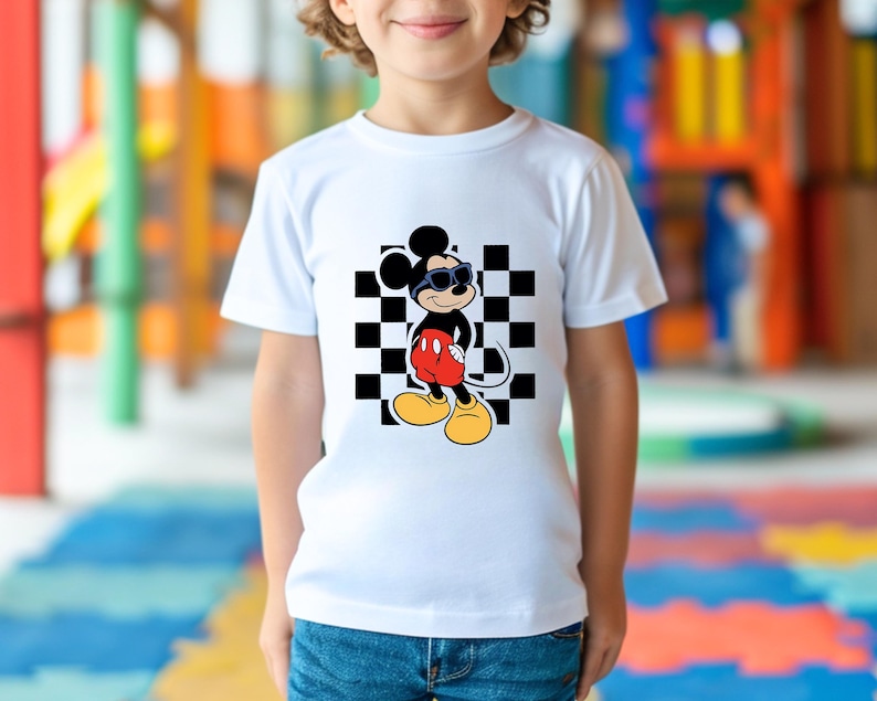 May include: White t-shirt with a black and white checkered background and a cartoon image of Mickey Mouse wearing sunglasses. Mickey Mouse is wearing red shorts and black shoes.