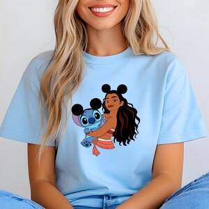 May include: Light blue t-shirt featuring a graphic of a cartoon character embracing a blue alien-like creature. The cartoon character has long dark hair and is wearing a red and white outfit. The alien has large eyes and ears.