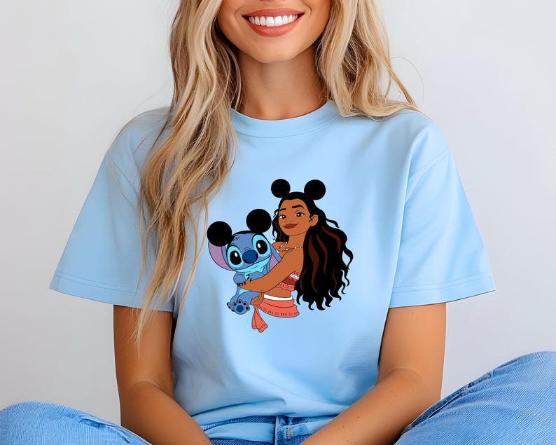 May include: Light blue t-shirt featuring a graphic of a cartoon character embracing a blue alien-like creature. The cartoon character has long dark hair and is wearing a red and white outfit. The alien has large eyes and ears.