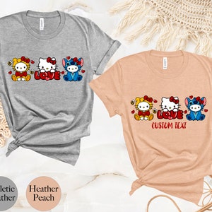 May include: Athletic heather and heather peach t-shirts featuring cartoon characters. The shirts display Hello Kitty, Stitch, and a bee character with the word "LOVE" in red. The peach shirt has "CUSTOM TEXT" below the word "LOVE".