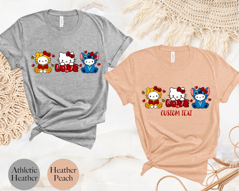 May include: Athletic heather and heather peach t-shirts featuring cartoon characters. The shirts display Hello Kitty, Stitch, and a bee character with the word "LOVE" in red. The peach shirt has "CUSTOM TEXT" below the word "LOVE".