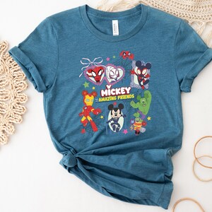 May include: Teal blue t-shirt featuring a graphic of Mickey Mouse and other characters. The graphic includes Spider-Man, Iron Man, and other characters with the text "Mickey Amazing Friends".