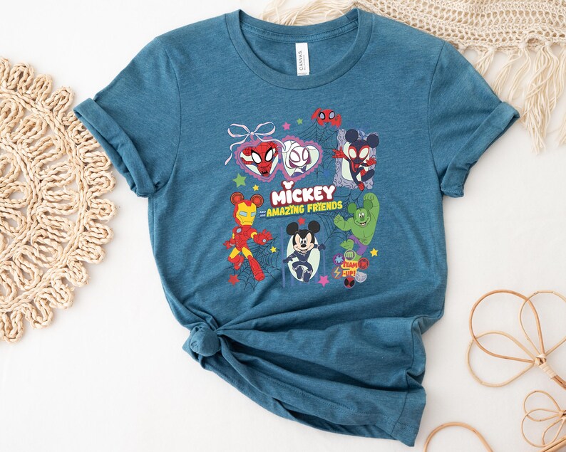 May include: Teal blue t-shirt featuring a graphic of Mickey Mouse and other characters. The graphic includes Spider-Man, Iron Man, and other characters with the text "Mickey Amazing Friends".