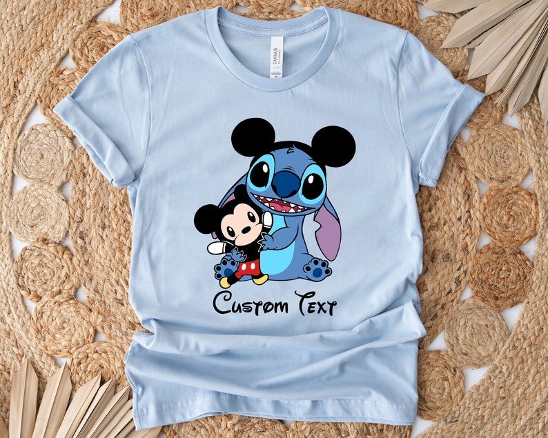 May include: Light blue t-shirt with a cartoon image of Stitch and Mickey Mouse. The text "Custom Text" is printed below the image.