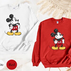 May include: Two sweatshirts with a cartoon drawing of Mickey Mouse. One sweatshirt is white and the other is red.
