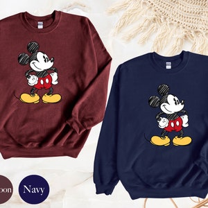 May include: Two sweatshirts with a cartoon drawing of Mickey Mouse. One sweatshirt is maroon and the other is navy blue.