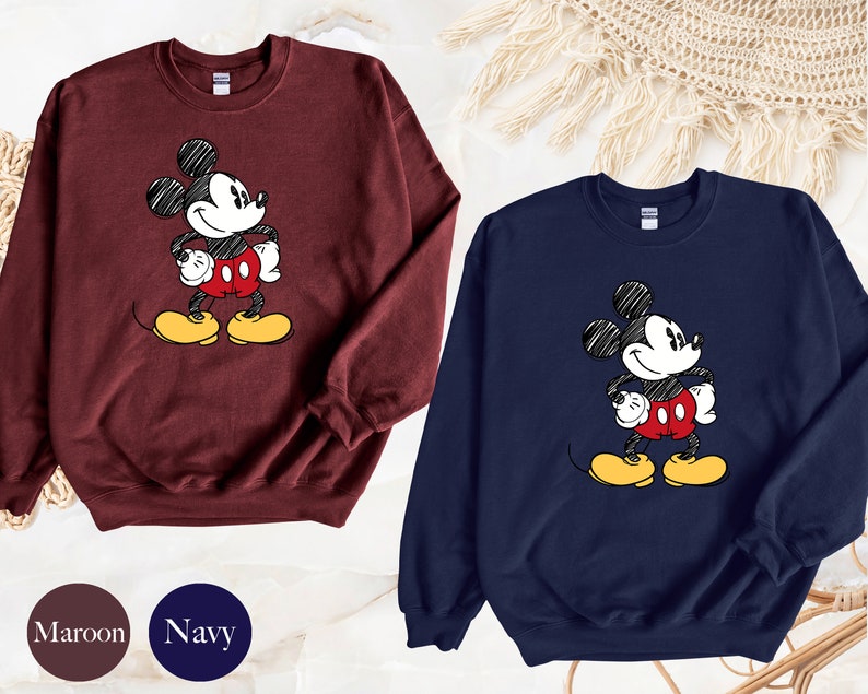 May include: Two sweatshirts with a cartoon drawing of Mickey Mouse. One sweatshirt is maroon and the other is navy blue.