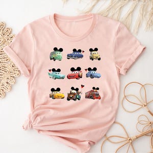 Puede incluir: Camiseta rosa con un estampado gr&aacute;fico de varios personajes de Cars de Disney con orejas de Mickey Mouse. Los personajes incluyen Mater, Rayo McQueen y Tow Mater.