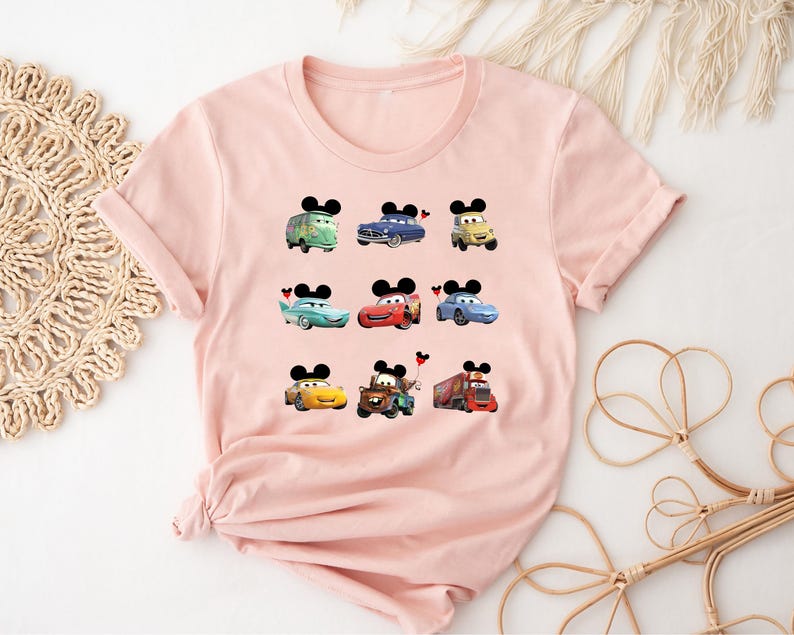 Puede incluir: Camiseta rosa con un estampado gr&aacute;fico de varios personajes de Cars de Disney con orejas de Mickey Mouse. Los personajes incluyen Mater, Rayo McQueen y Tow Mater.