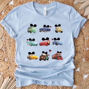Puede incluir: Camiseta azul claro con un gr&aacute;fico de varios personajes de Cars de la pel&iacute;cula Cars de Disney Pixar. Los personajes incluyen Rayo McQueen, Mate y otros. Cada personaje tiene orejas de Mickey Mouse.
