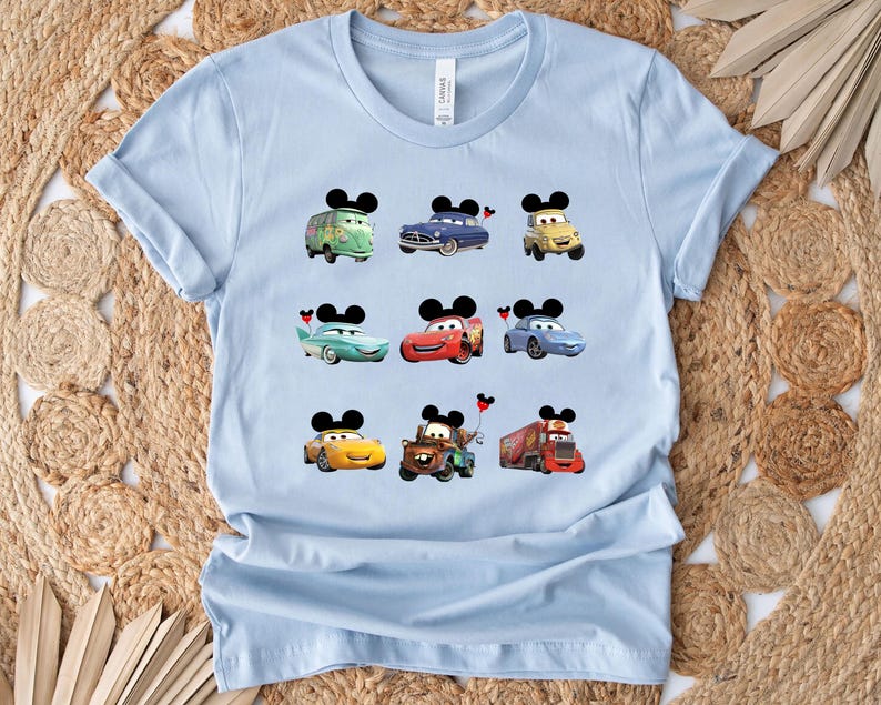 Puede incluir: Camiseta azul claro con un gr&aacute;fico de varios personajes de Cars de la pel&iacute;cula Cars de Disney Pixar. Los personajes incluyen Rayo McQueen, Mate y otros. Cada personaje tiene orejas de Mickey Mouse.