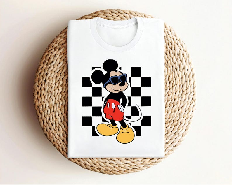 May include: White t-shirt with a black and white checkered pattern and a cartoon image of Mickey Mouse wearing sunglasses. Mickey Mouse is standing with his hands on his hips.
