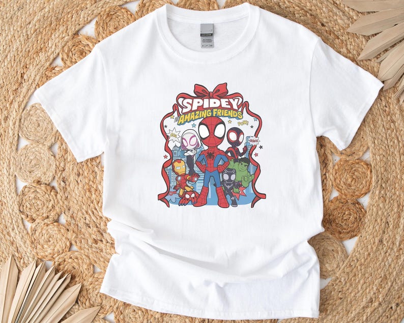 以下が含まれることがあります： スパイディとアメイジング・フレンズのカラフルなグラフィックが特徴の白いTシャツ。デザインにはスパイダーマン、アイアンマン、その他のキャラクターが含まれています。「Spidey Amazing Friends」の文字がキャラクターの上に表示されています。