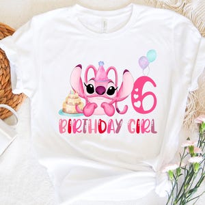 May include: White t-shirt with a pink Stitch character wearing a birthday hat and holding a cake. The number 6 and the words "Birthday Girl" are printed on the shirt.