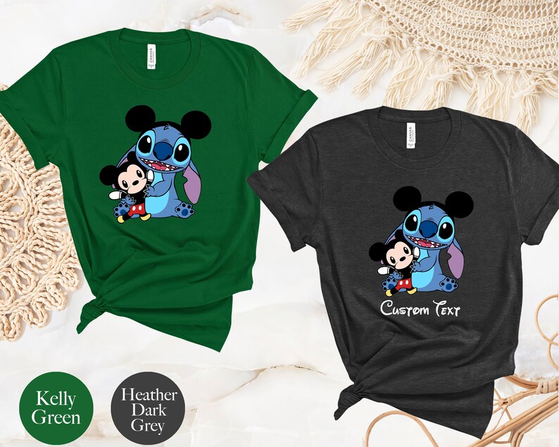 May include: Two t-shirts with a cartoon image of Stitch from Lilo & Stitch holding Mickey Mouse. The shirt on the left is Kelly green and the shirt on the right is heather dark grey. The text "Custom Text" is printed on the grey shirt.