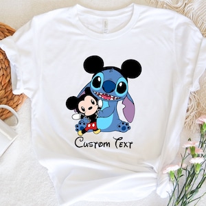 May include: White t-shirt with a blue Stitch character holding a Mickey Mouse character. The text "Custom Text" is printed below the characters.