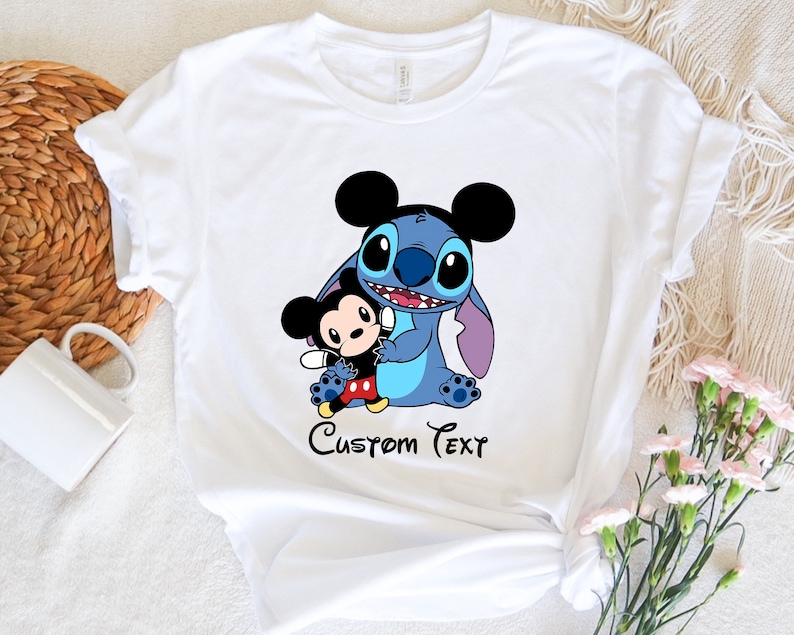 May include: White t-shirt with a blue Stitch character holding a Mickey Mouse character. The text "Custom Text" is printed below the characters.