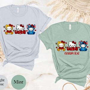 May include: Light blue and mint green t-shirts featuring cartoon characters. The light blue shirt has a bee-themed Hello Kitty, Hello Kitty with the word "LOVE", and Stitch. The mint green shirt has the text "CUSTOM TEXT".