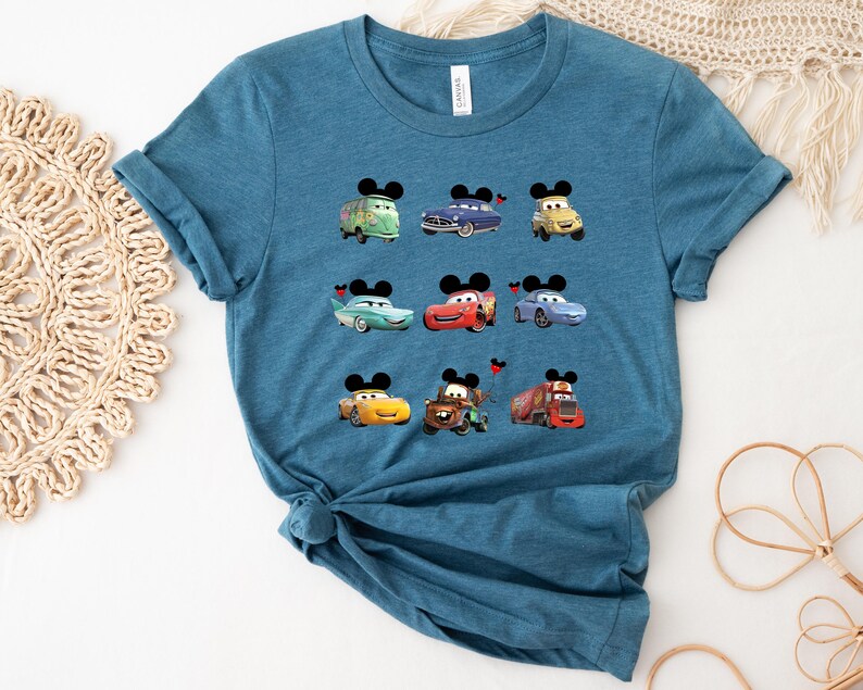 Puede incluir: Una camiseta azul turquesa con un estampado gr&aacute;fico de nueve coches de dibujos animados con orejas de Mickey Mouse. Los coches son rojos, azules, verdes y amarillos.