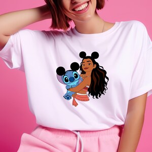 May include: White t-shirt featuring a cartoon graphic of Moana and Stitch. Moana is wearing a red and white outfit and holding Stitch, who is blue. The shirt has a crew neck and short sleeves.