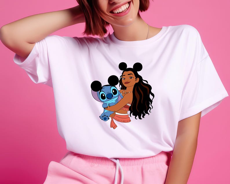 May include: White t-shirt featuring a cartoon graphic of Moana and Stitch. Moana is wearing a red and white outfit and holding Stitch, who is blue. The shirt has a crew neck and short sleeves.