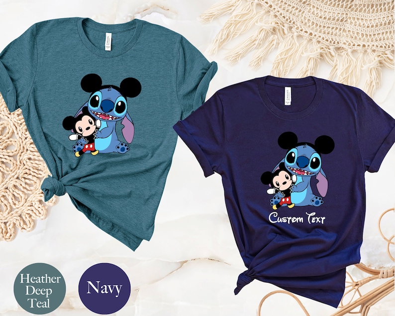 May include: Two t-shirts featuring a cartoon image of Stitch from Lilo & Stitch hugging Mickey Mouse. The shirt on the left is a heather deep teal color. The shirt on the right is navy blue and has the text "Custom Text" printed below the image.