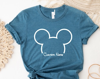 May include: A teal blue t-shirt with a white outline of Mickey Mouse's ears and the text "Custom Name" underneath.